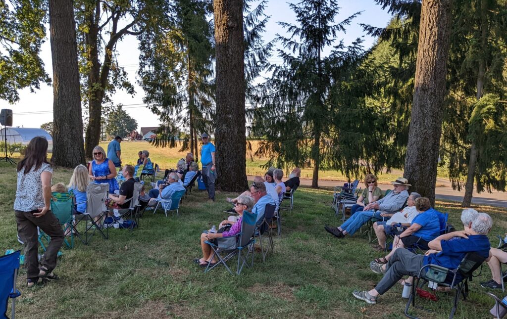 Image of a bluegrass concert held on the lawn behind Rosedale Friends Church underneath tall trees