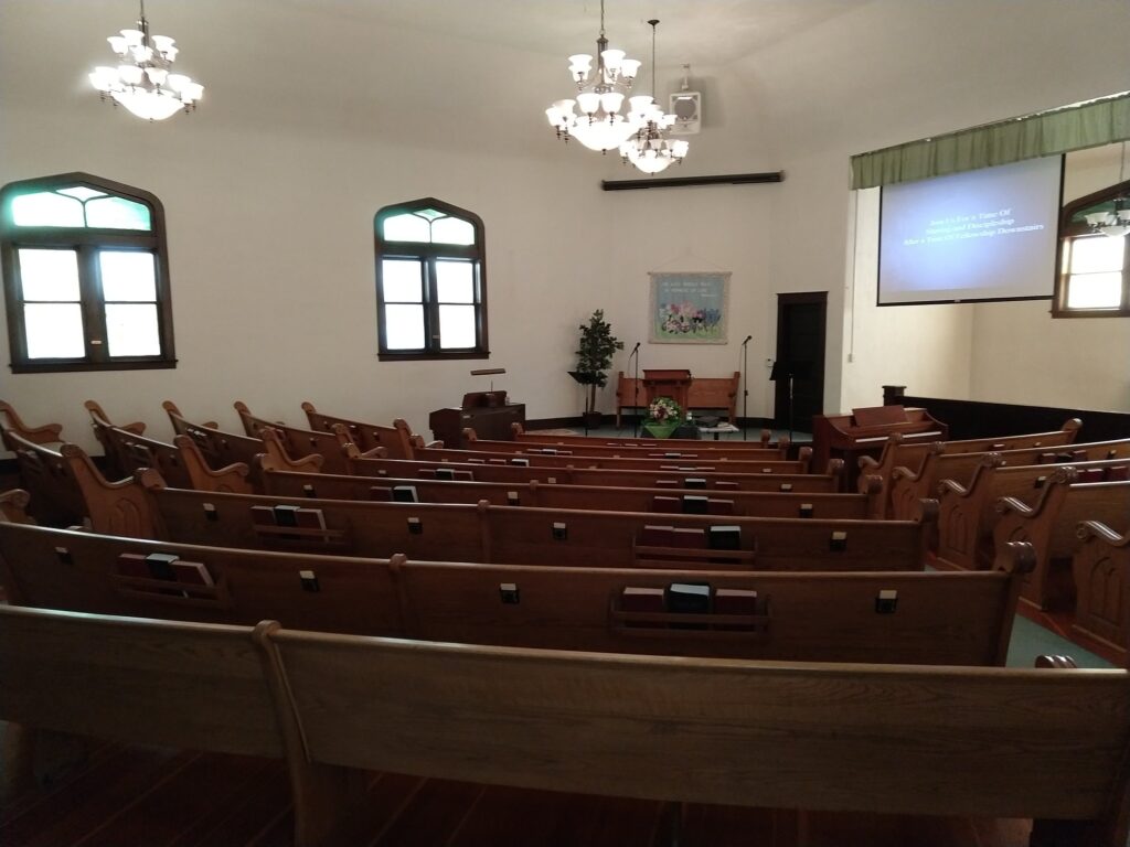 The sanctuary at Rosedale Friends Church. It contains rows of wooden pews and stained glass windows